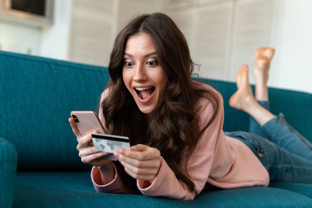 Woman using mobile phone holding credit card on sofa.